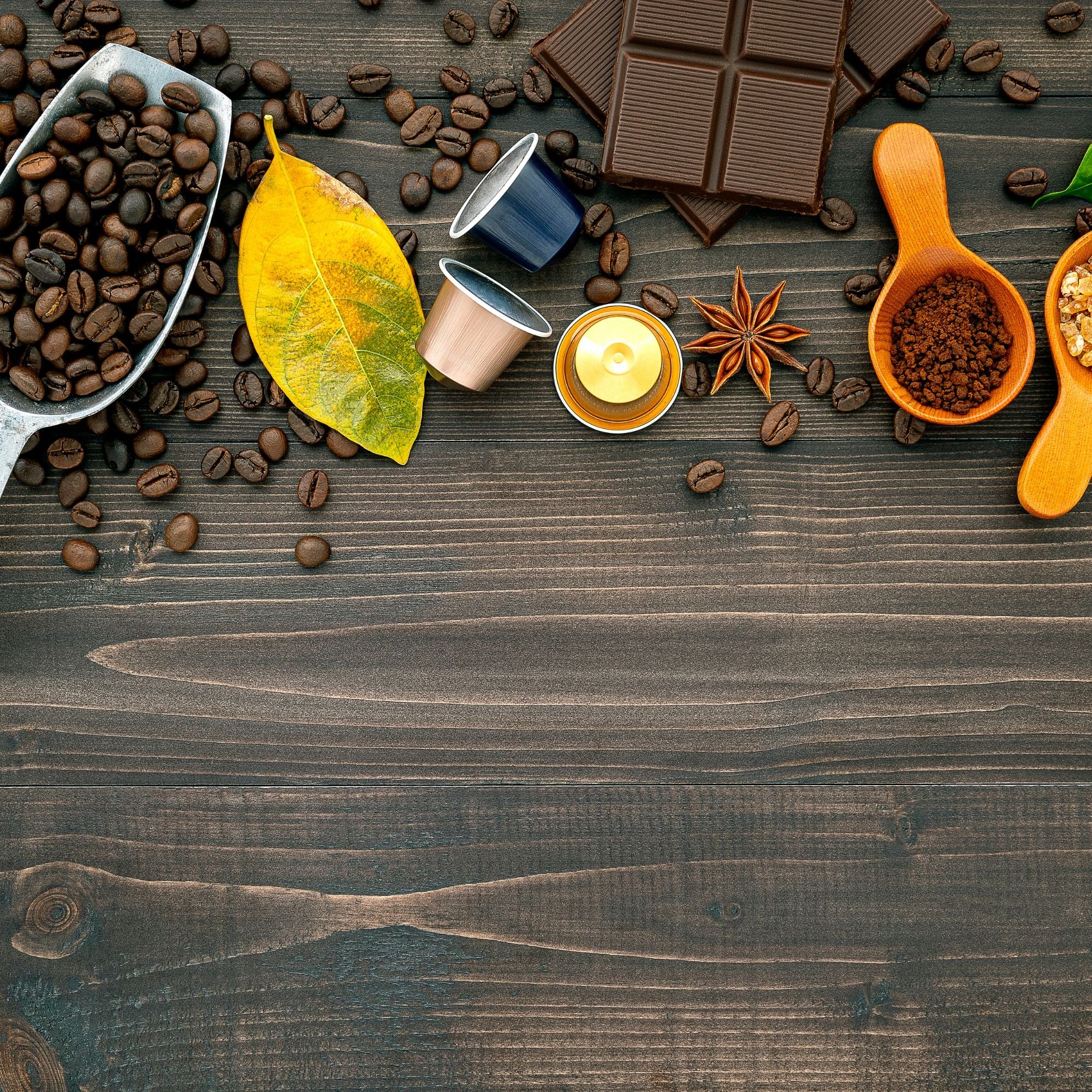Coffee beans, chocolate, and spices arranged on a dark wooden surface with a yellow leaf.